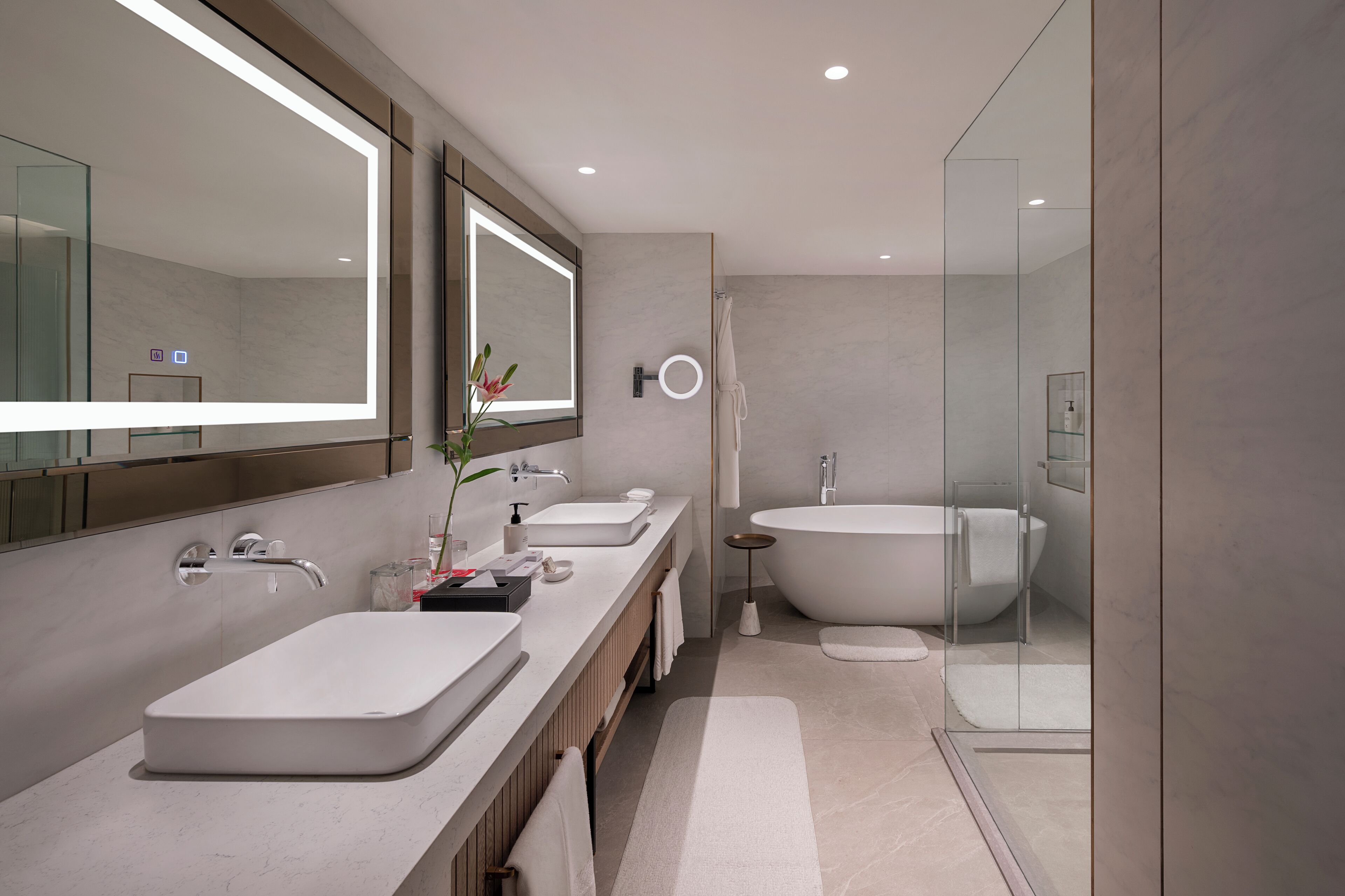 A modern bathroom with a large mirror, two sinks, a bathtub, and a glass shower enclosure.