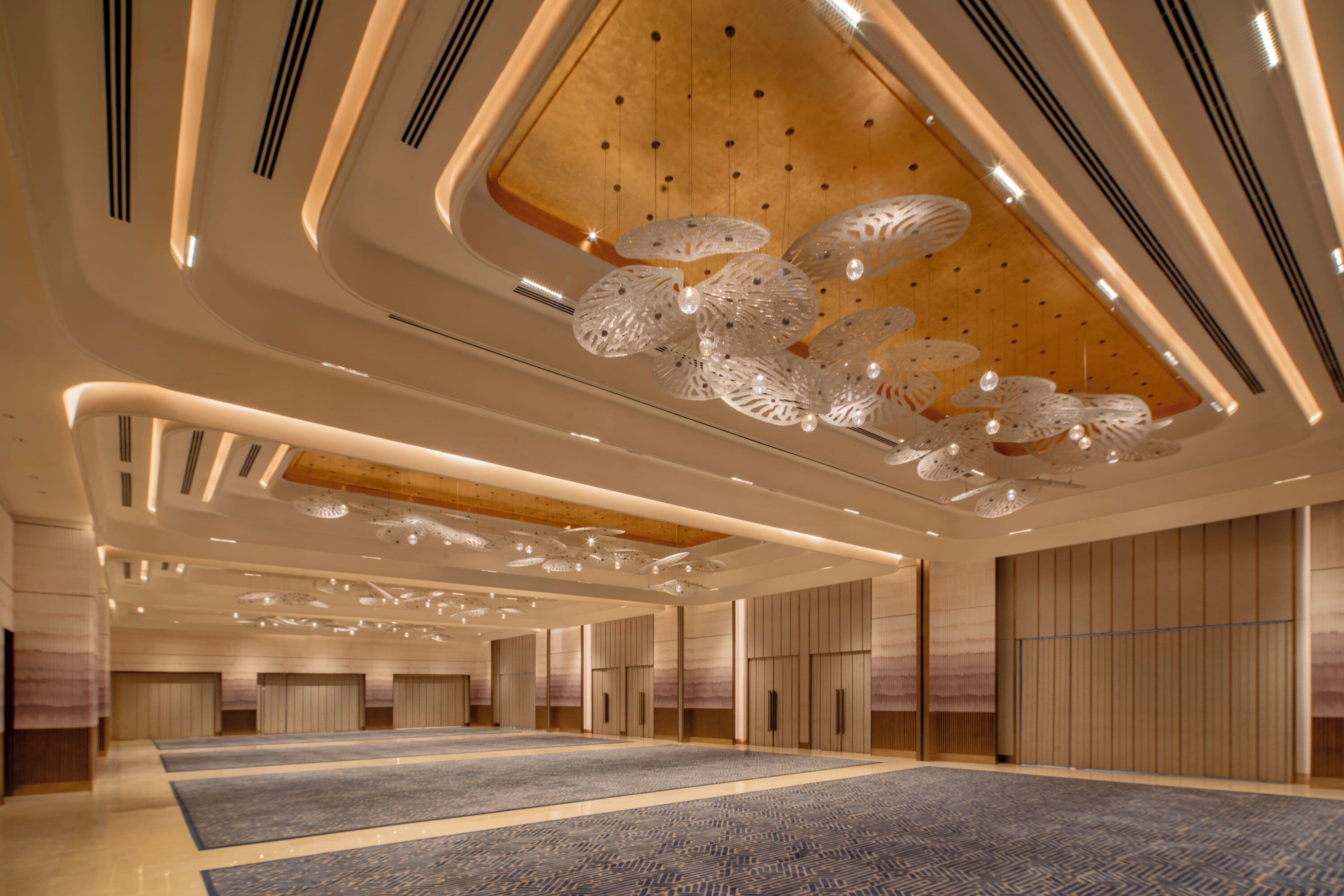 Un amplio vestíbulo de hotel con una gran área alfombrada, techo de madera e iluminación moderna.