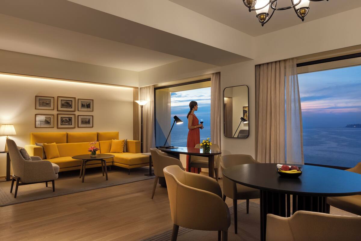Une chambre d’hôtel moderne dotée d’une grande fenêtre, d’un canapé, d’une table à manger et d’un lampadaire.