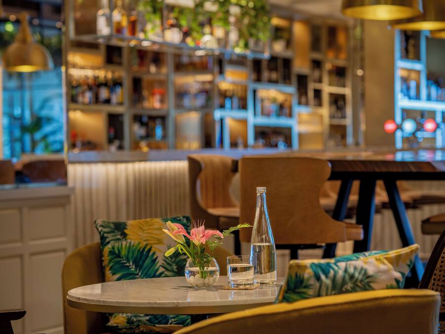 A bar area with a round table, chairs, a bottle, and a glass.