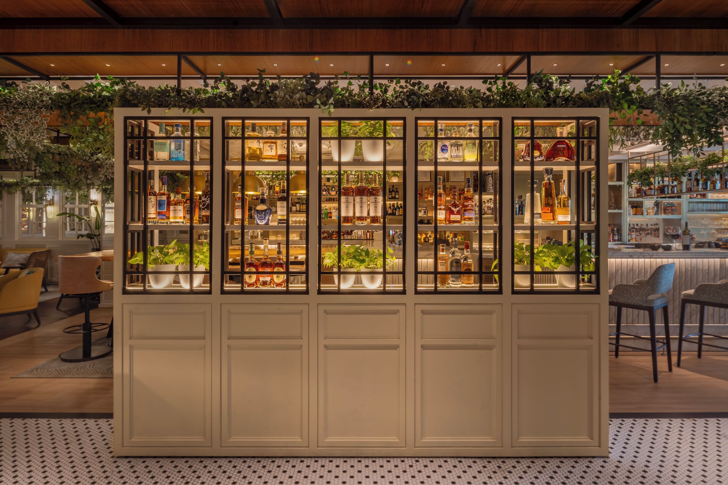 A bar area with shelves of bottles, a seating area with chairs, and a decorative plant wall.