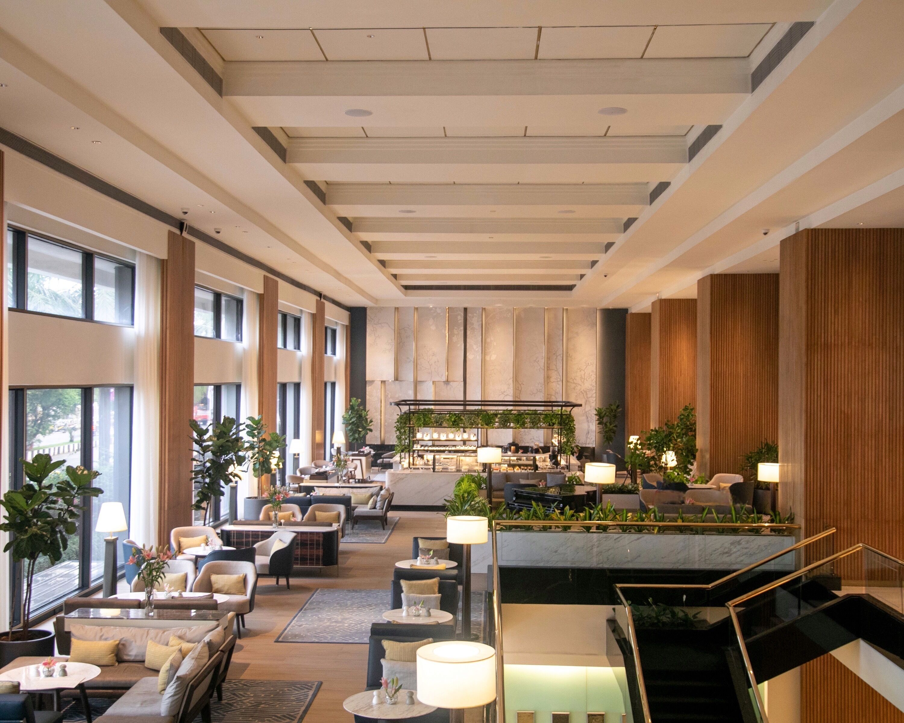 A spacious hotel lobby with high ceilings, large windows, and a central seating area with sofas and tables.