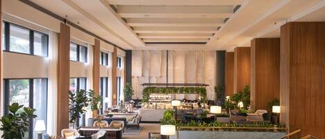 Un'ampia hall d'albergo con soffitti alti, grandi finestre e un'area salotto centrale con divani e tavolini.