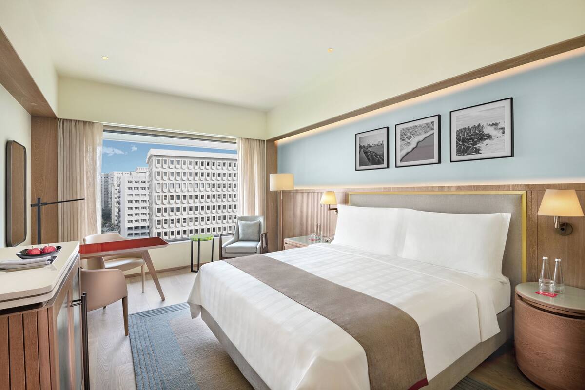 Une chambre d’hôtel avec un lit, un bureau, une chaise et une vue sur les bâtiments.