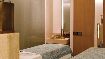 Two single beds with white linens and a runner, a nightstand with a mirror and a vase, and a large mirror on the wall.