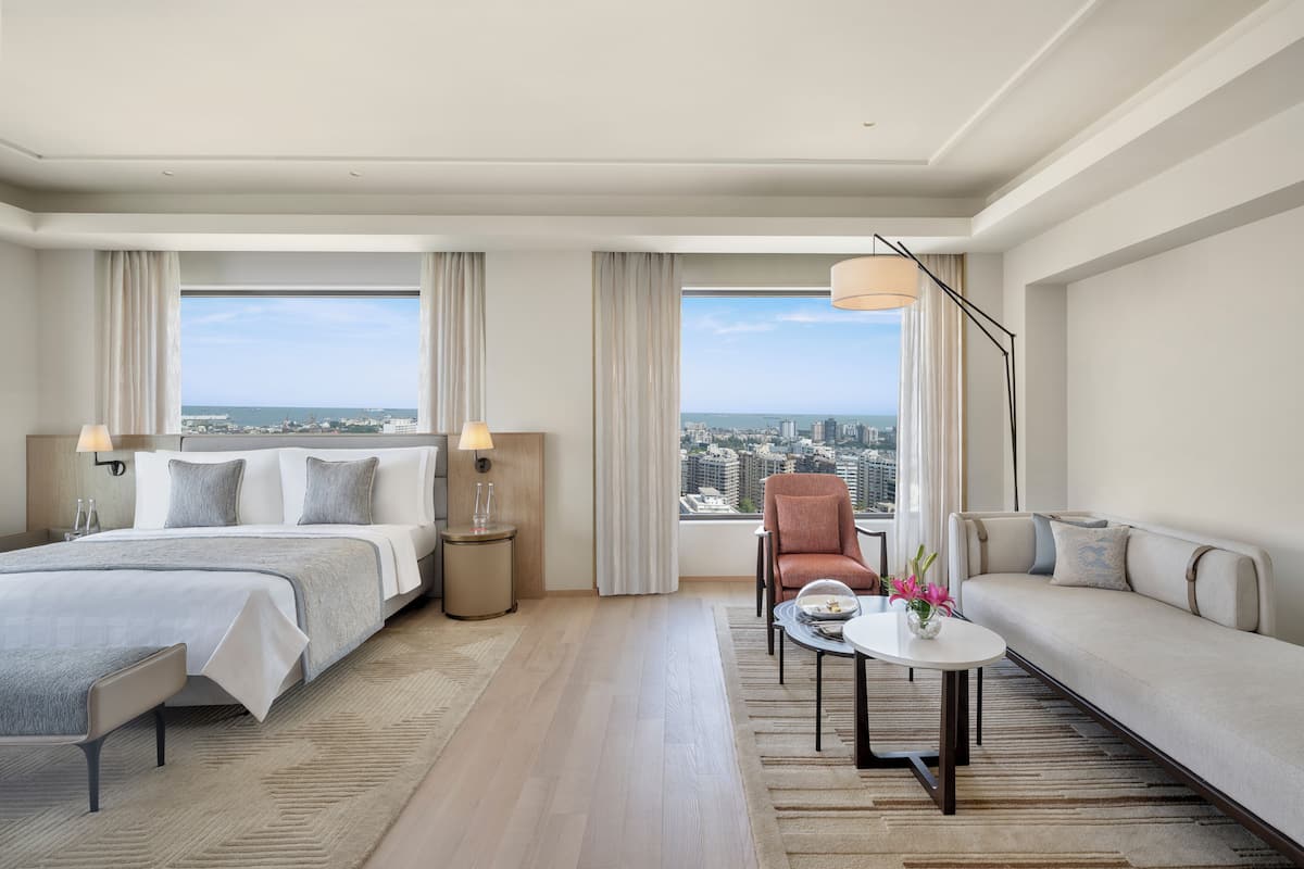 Une chambre d’hôtel avec un lit, un canapé, une chaise, une petite table et une vue sur la ville.