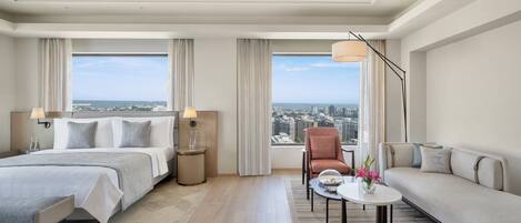 Habitación de hotel con cama, sofá, sillón, mesita y vistas a la ciudad.