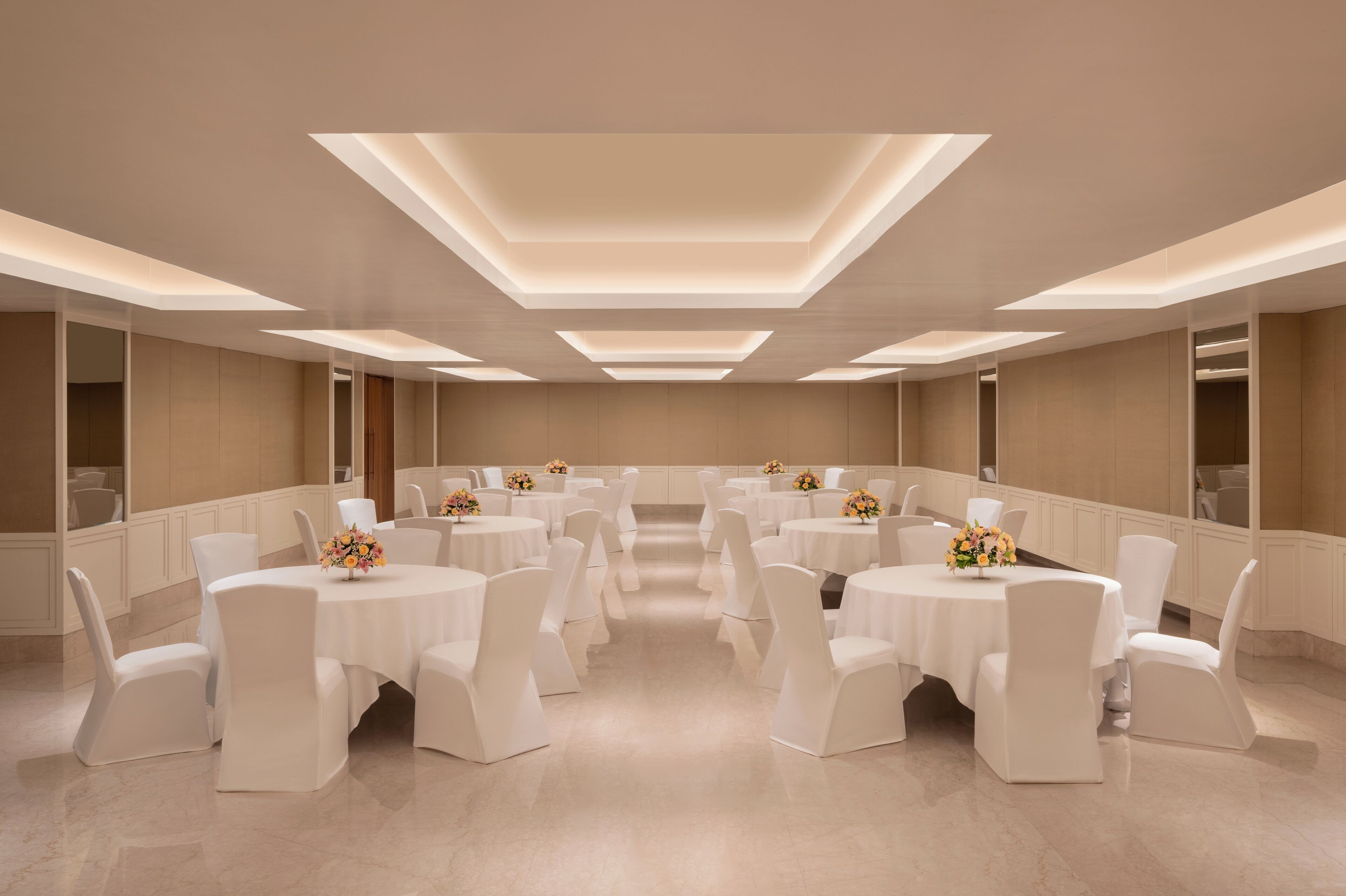 A spacious room with multiple round tables and white chairs, arranged in a symmetrical layout.