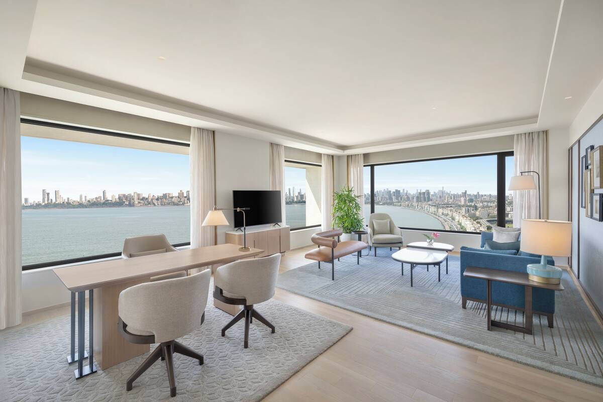 Une chambre d’hôtel moderne avec vue sur la ville, une télévision à écran plat, un coin repas et un espace salon avec un canapé et des fauteuils.