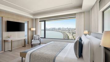 A modern hotel room with a large bed, a flat-screen TV, a desk, and a large window offering a city view.