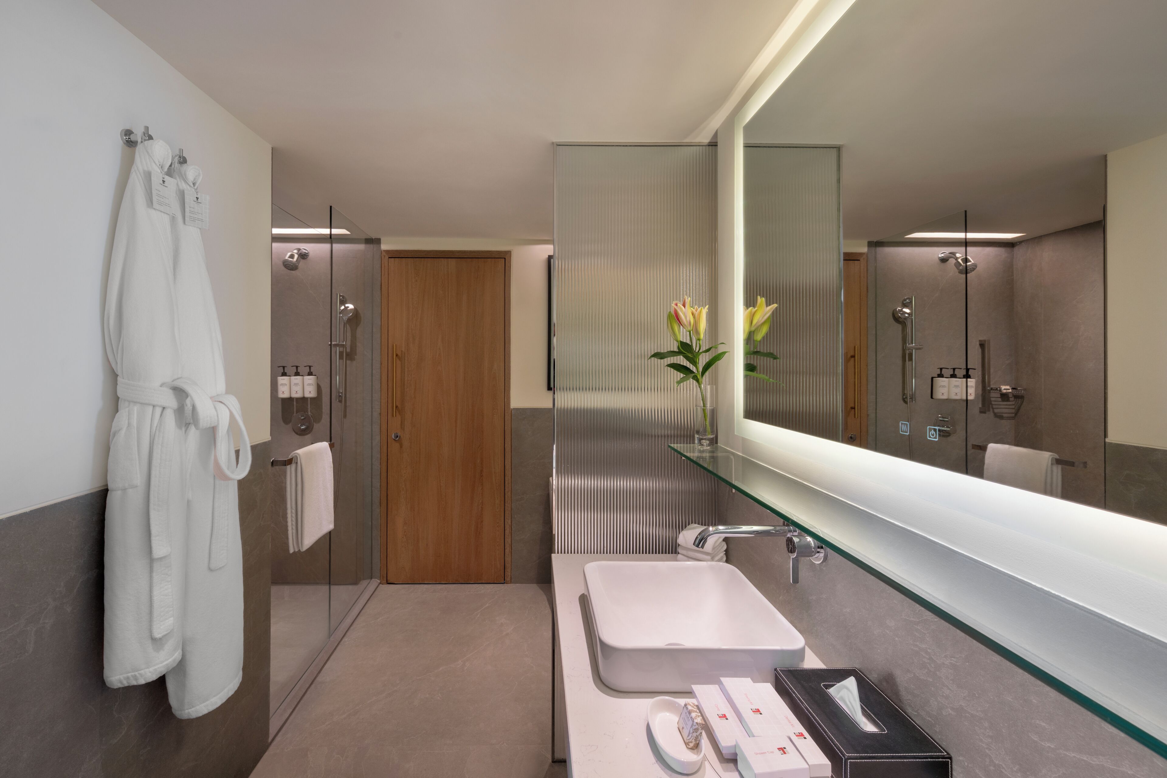 Un baño moderno con cabina de ducha de vidrio, un espejo grande y un lavabo blanco.
