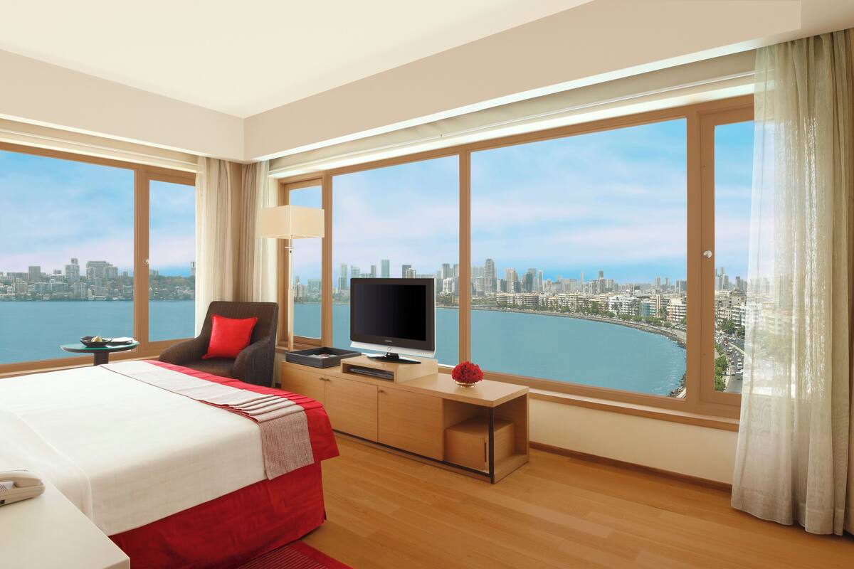 Une chambre d’hôtel avec un grand lit, une télévision, un bureau et une vue sur les toits de la ville et sur l’eau.