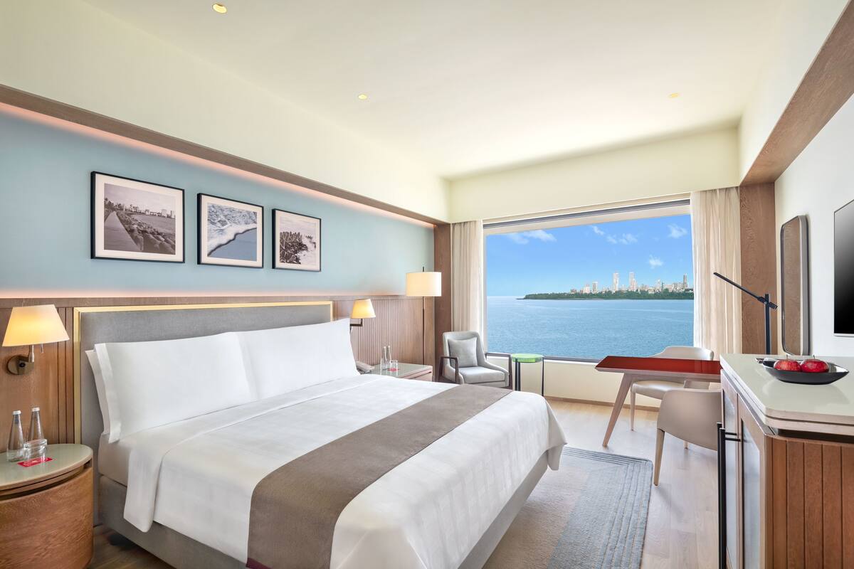 Une chambre d’hôtel avec un grand lit, un bureau, une chaise et une vue sur la mer.