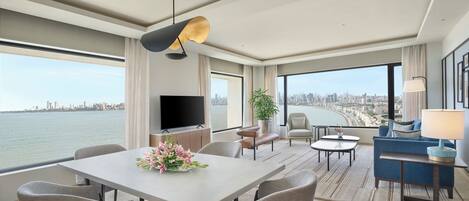Una moderna camera d'hotel con zona pranzo, posti a sedere, televisione e un'ampia finestra vista città.