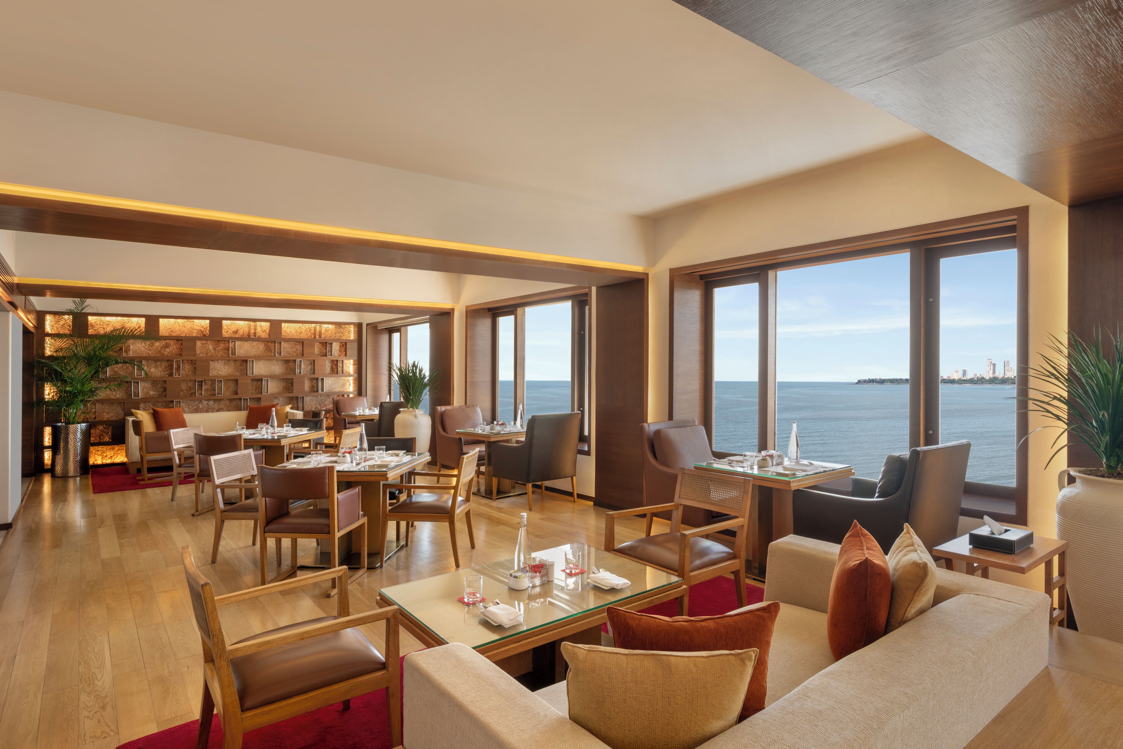 A spacious hotel lobby with a dining area, seating arrangements, and large windows offering a view of the sea.