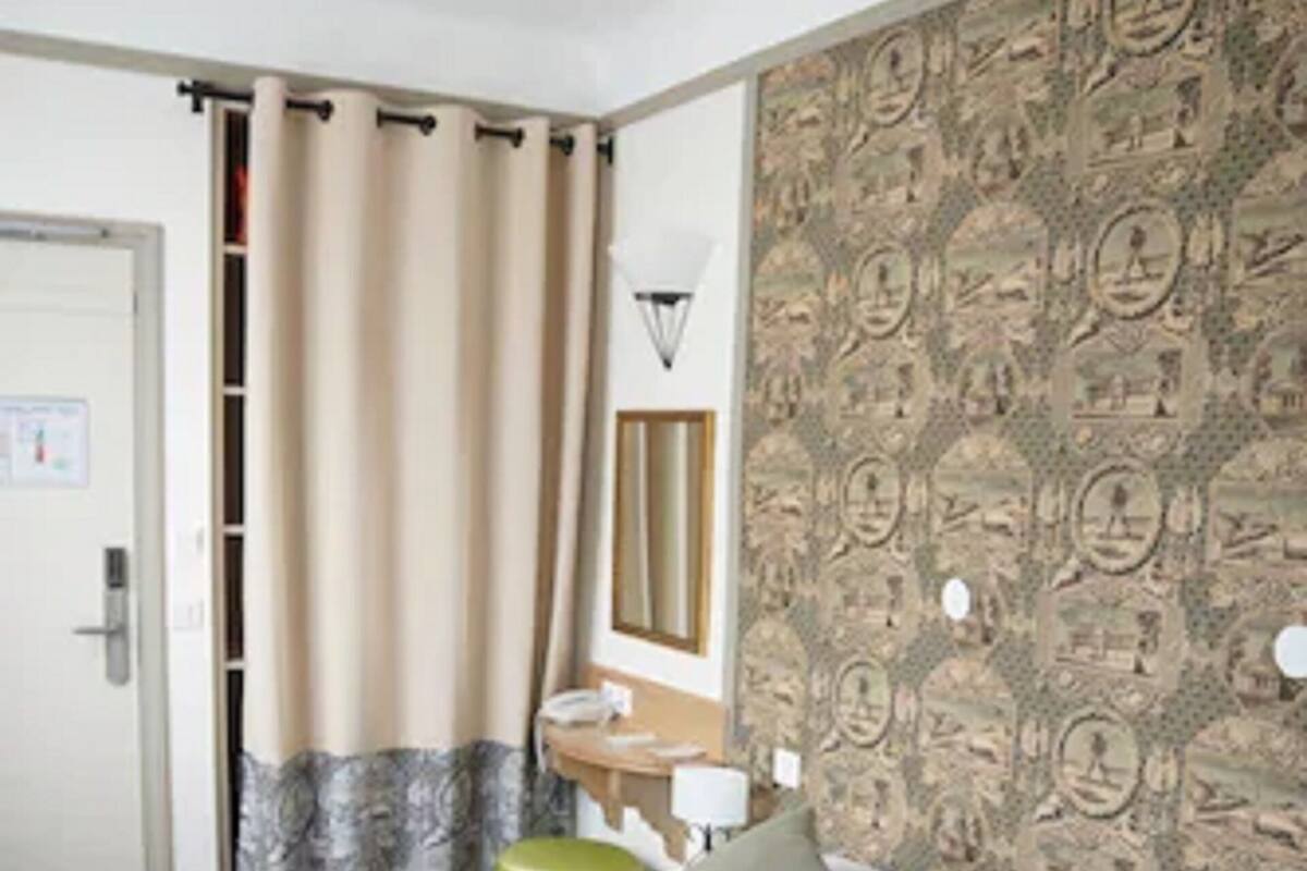 Une chambre d’hôtel avec un lit, un miroir, une table de chevet et un papier peint à motifs.