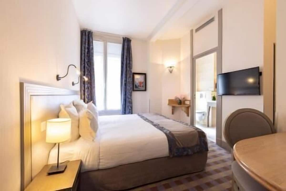 Une chambre d’hôtel avec un lit, une lampe de chevet, une télévision et une petite table.