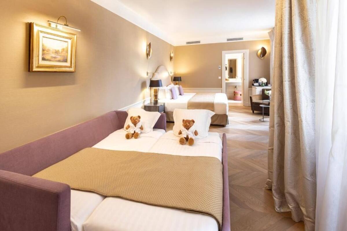 Une chambre d’hôtel avec un lit, un canapé, un bureau et une chaise. Il y a deux ours en peluche sur le lit.