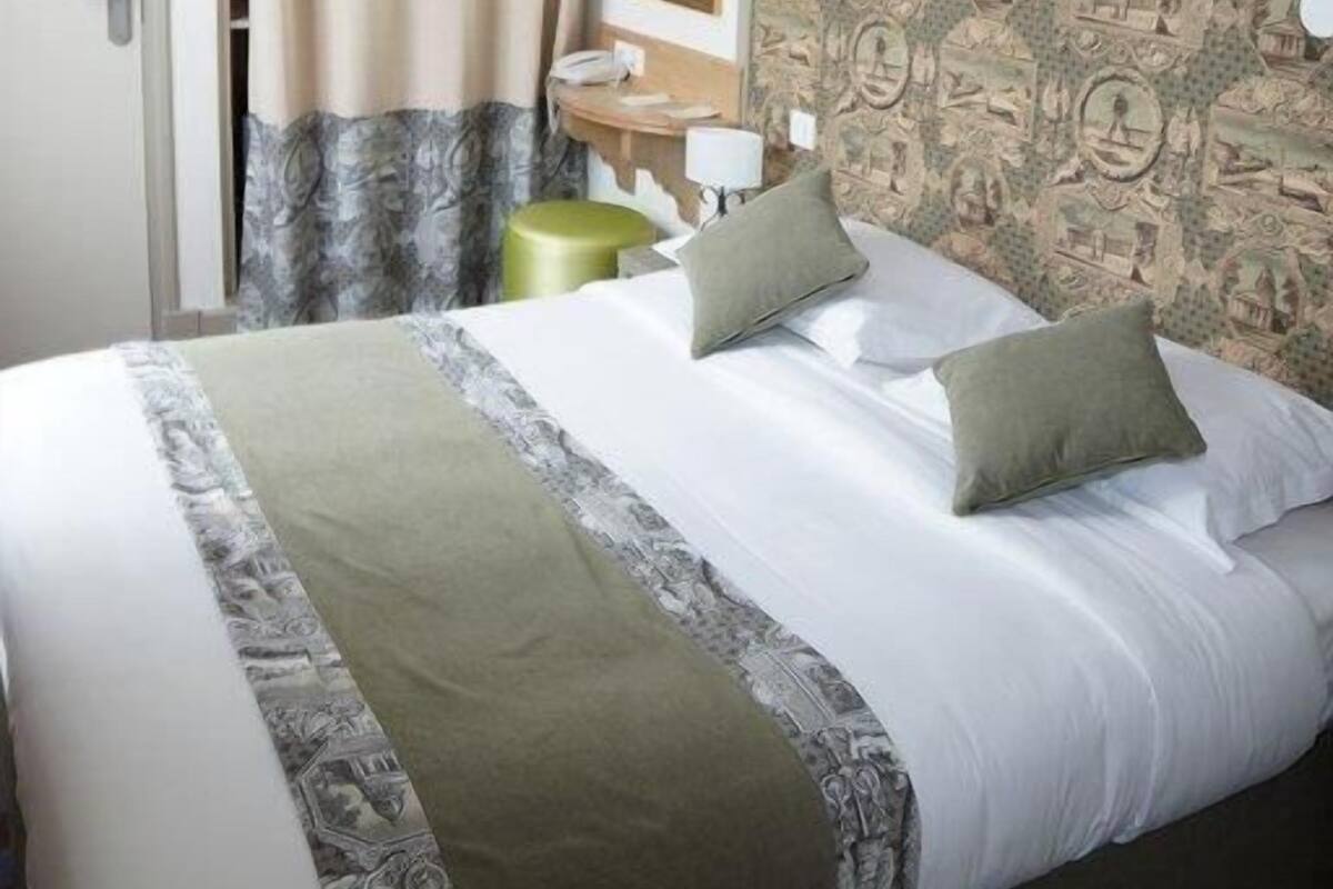 Une chambre d’hôtel avec un lit, une table de chevet, une lampe et un papier peint à motifs.