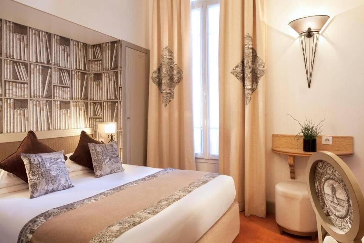 Une chambre d’hôtel avec un grand lit, une bibliothèque, une lampe fixée au mur et une petite table sur laquelle est posée une plante.