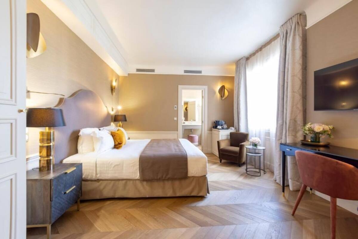 Une chambre d’hôtel avec un lit, un bureau, une chaise et un téléviseur fixé au mur.