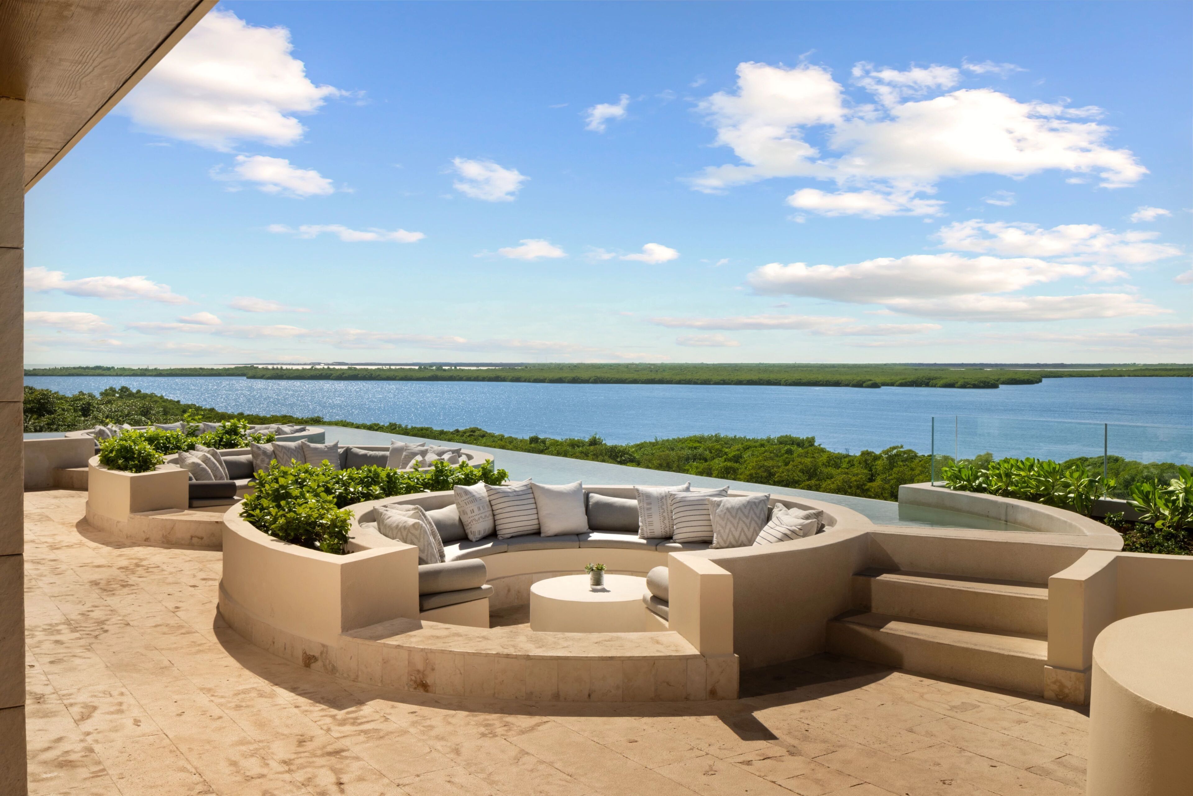 Uma área de estar ao ar livre circular com piscina, com vista para um corpo d'água e terras distantes.