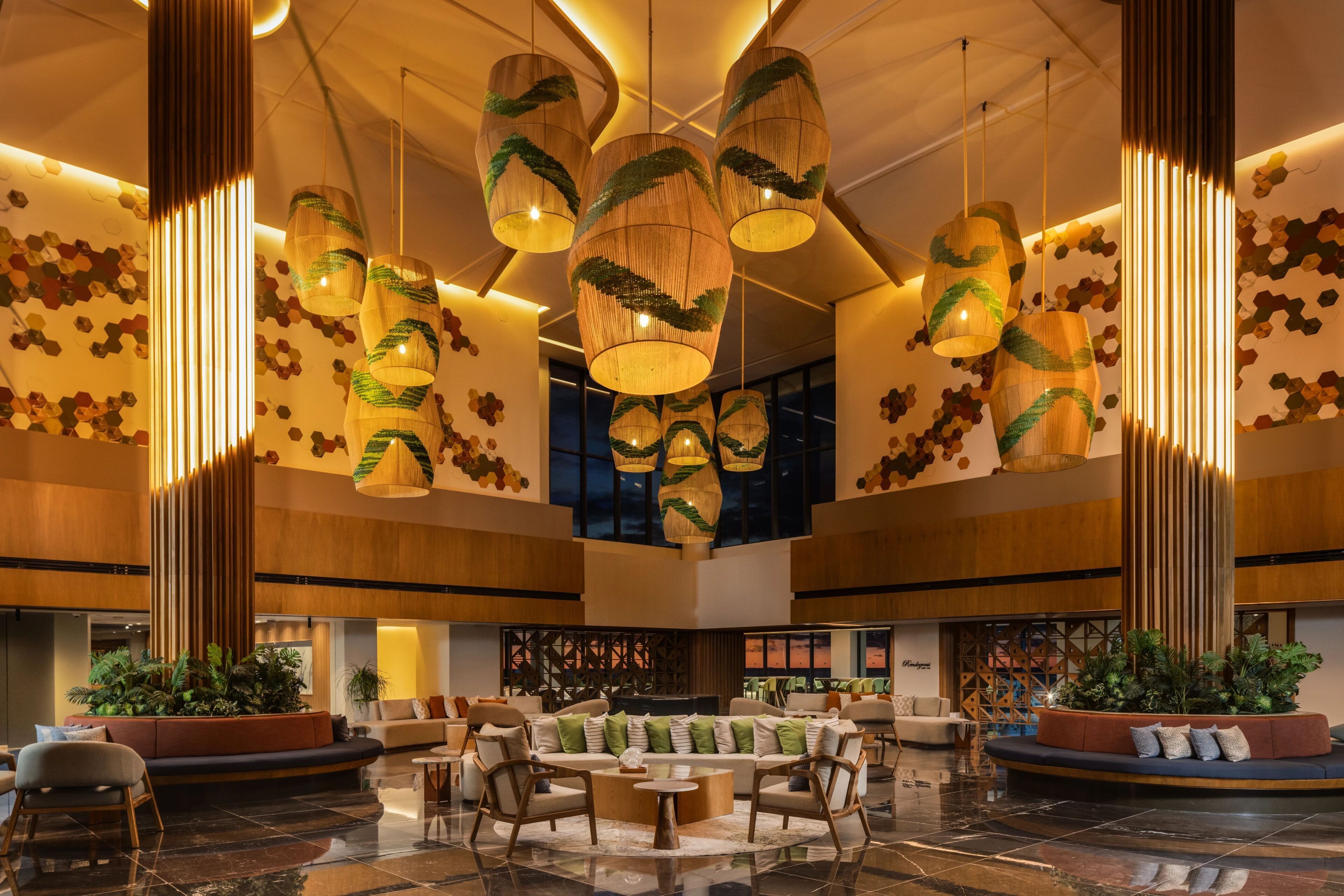 A spacious lobby with a central seating area, multiple hanging pendant lights, and a large window providing a view of the desert.