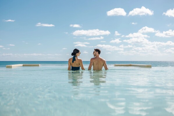 A couple in a clear infinity pool with a view of the ocean.