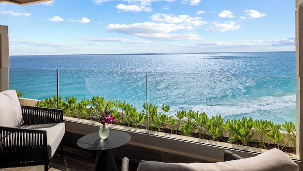 A balcony with a view of the ocean, a round table, and two chairs.