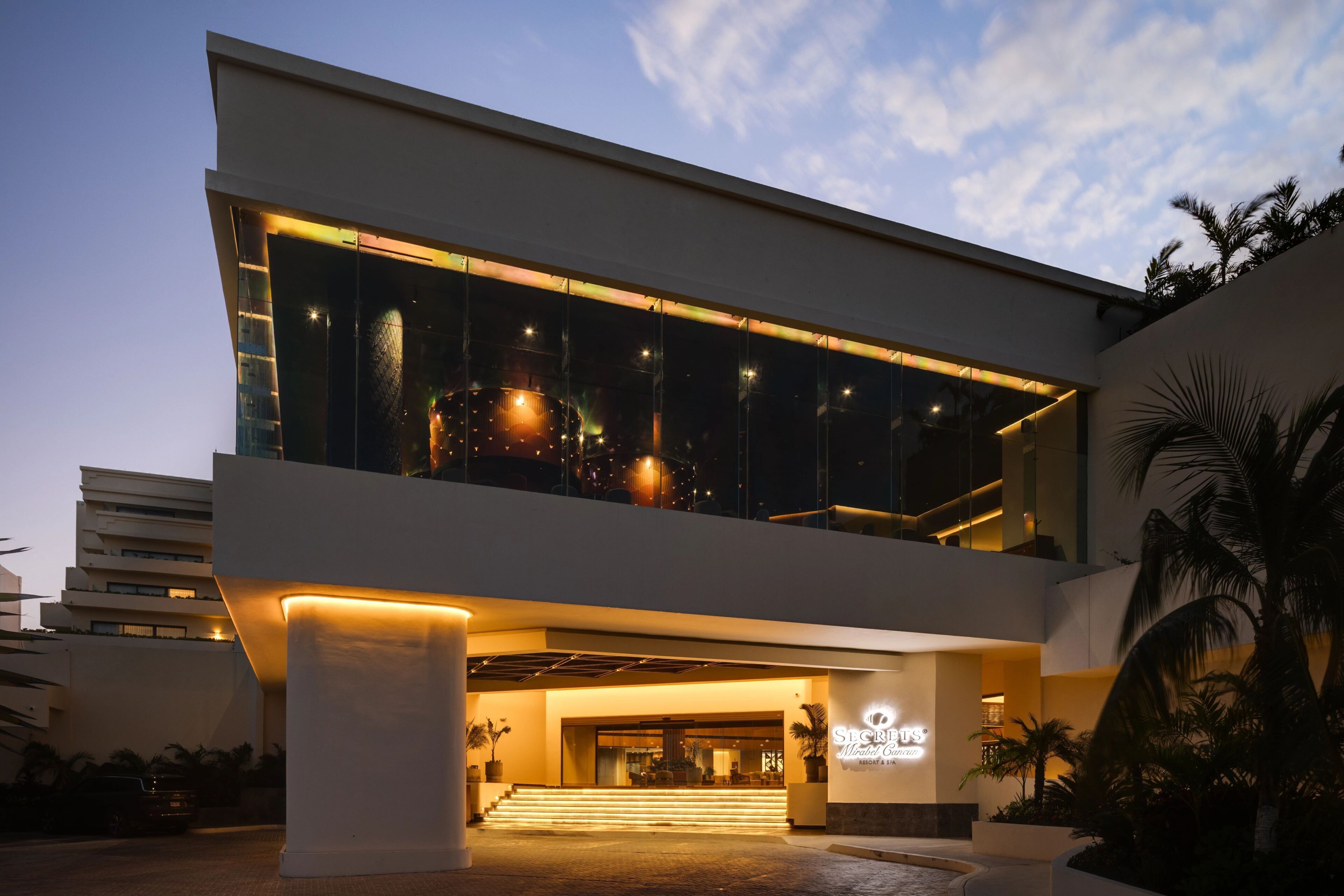 A modern hotel with a glass facade, a well-lit entrance, and a visible name sign.