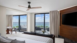 Une chambre d’hôtel avec un grand lit, un ventilateur de plafond, une télévision et un balcon offrant une vue sur l’océan.