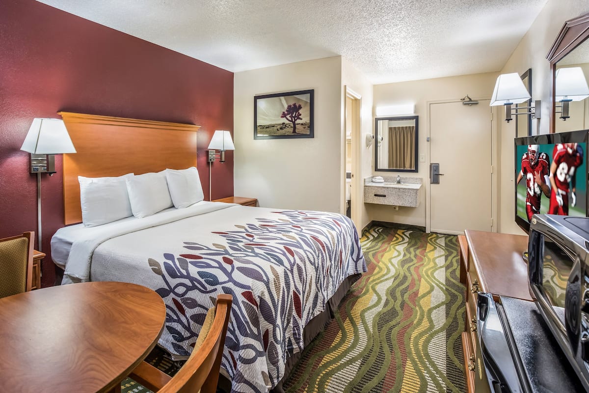 A hotel room with a bed, a TV, a desk, and a bathroom.