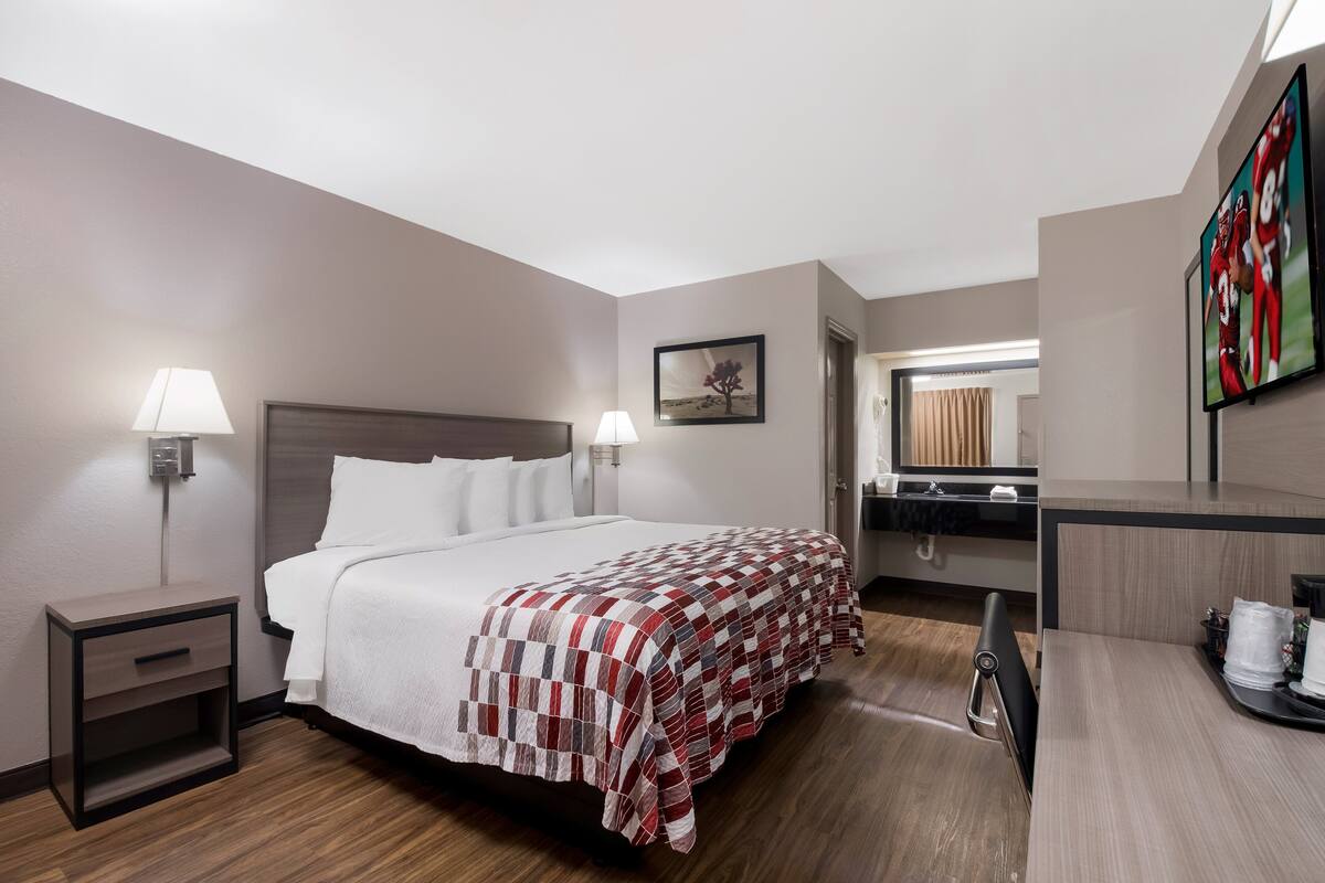 A hotel room with a bed, bedside tables, a desk, and a mirror.