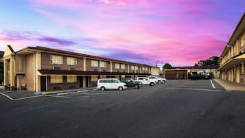 Un motel avec une rangée de places de stationnement et une rangée de chambres au rez-de-chaussée.