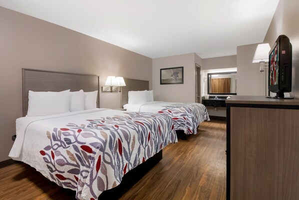Habitación de hotel con dos camas, un escritorio, un televisor y un baño visible a través de una puerta abierta.
