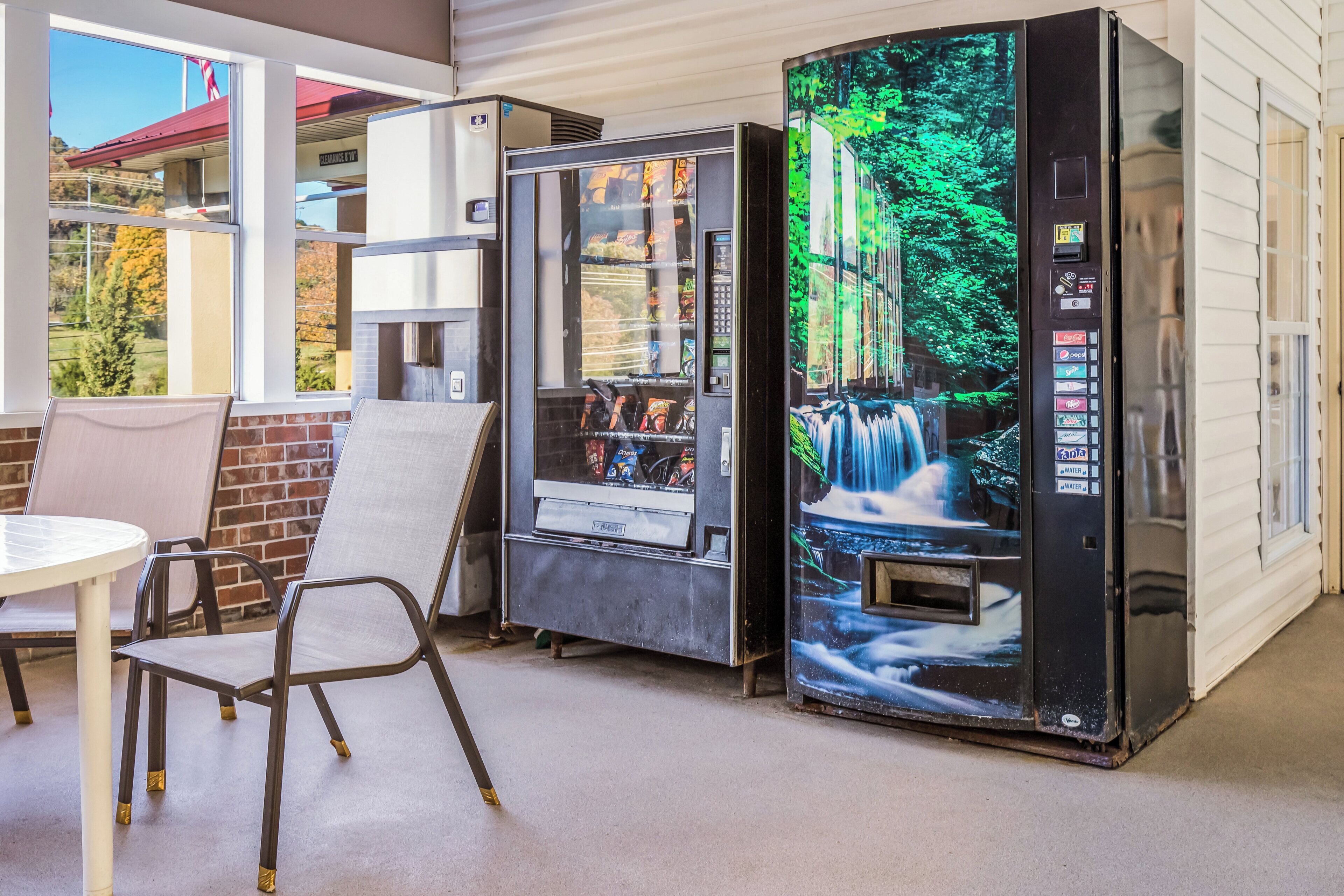 A vending machine with a waterfall display, a chair, and a table in a room with a window.