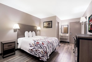 Habitación de hotel con cama, lámparas de noche, un cuadro, baño con lavabo y espejo, y televisor.