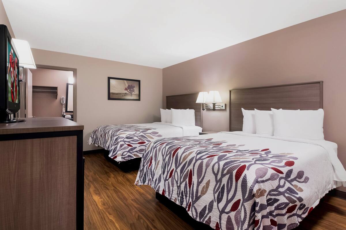 A hotel room with two beds, a desk, a mirror, and a lamp.