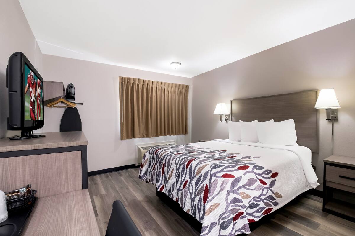 A hotel room with a bed, a desk, a television, and a lamp.