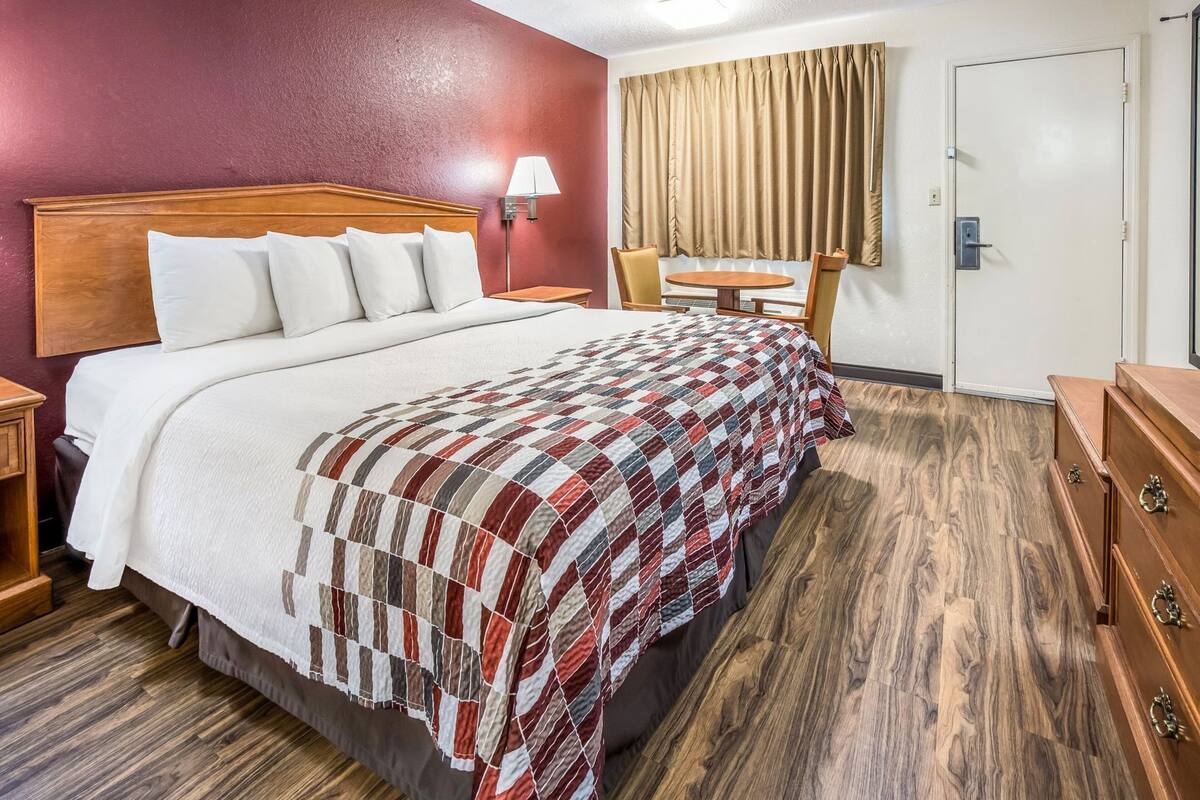 A hotel room with a bed, a desk, a chair, a lamp, and a window with curtains.