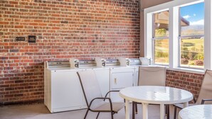 A room with a brick wall, a window with a view, a table, chairs, and a washing machine. - Red Roof Inn Chattanooga - Lookout Mountain (Chattanooga)
