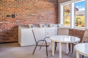 Una habitación con pared de ladrillo, ventana con vistas, una mesa, sillas y una lavadora.