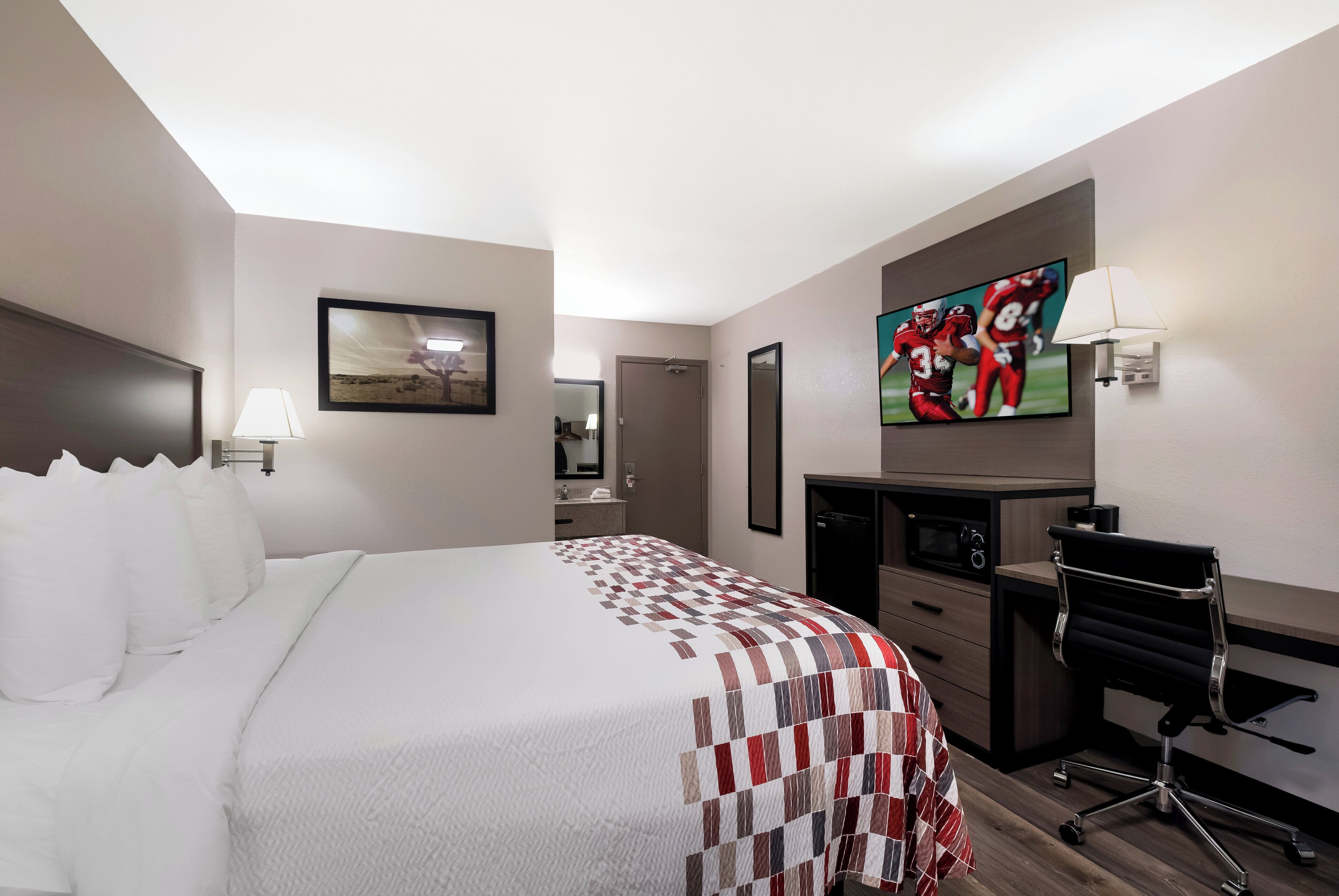 A hotel room with a bed, a desk, a TV, and a mirror.