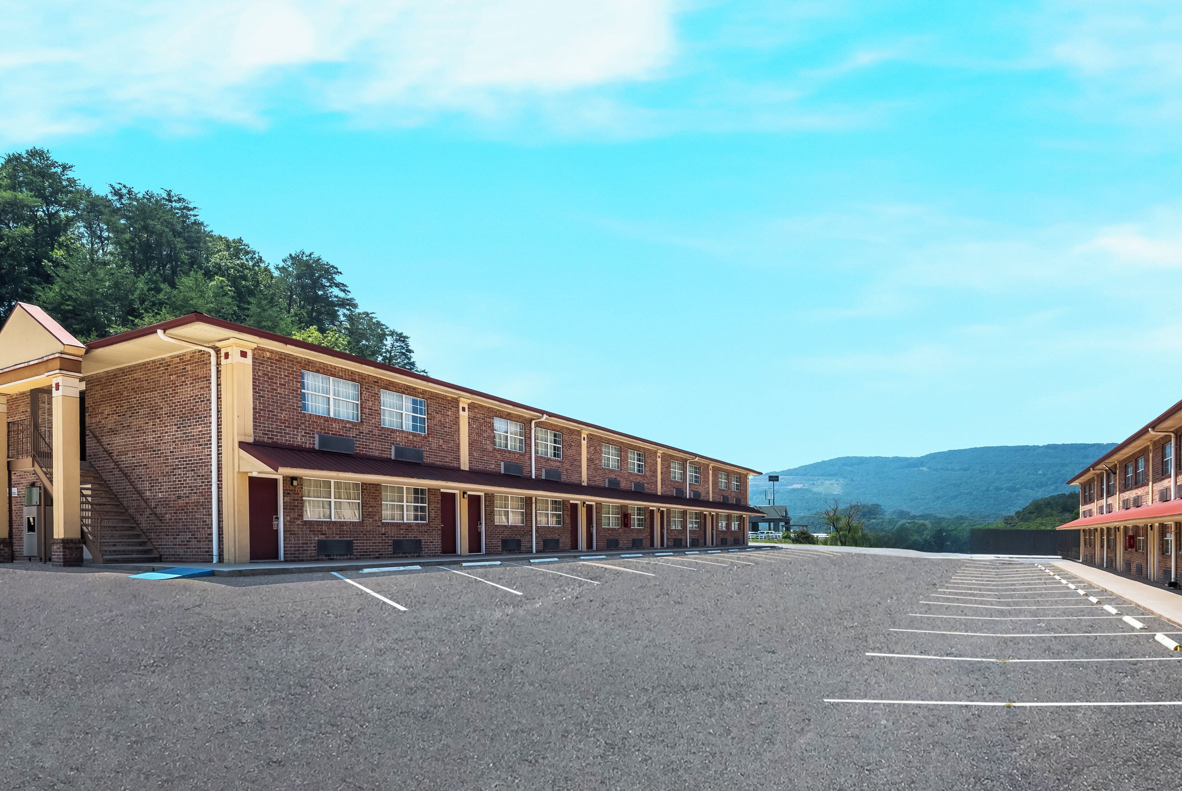 A motel with a parking lot and a mountain view in the background.