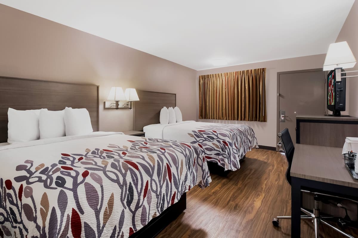 A hotel room with two beds, a desk, and a television.