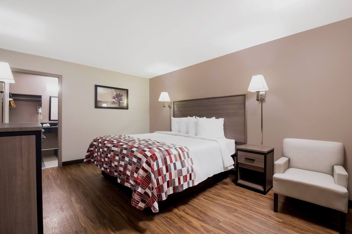 A hotel room with a bed, bedside tables, a chair, and a painting on the wall.