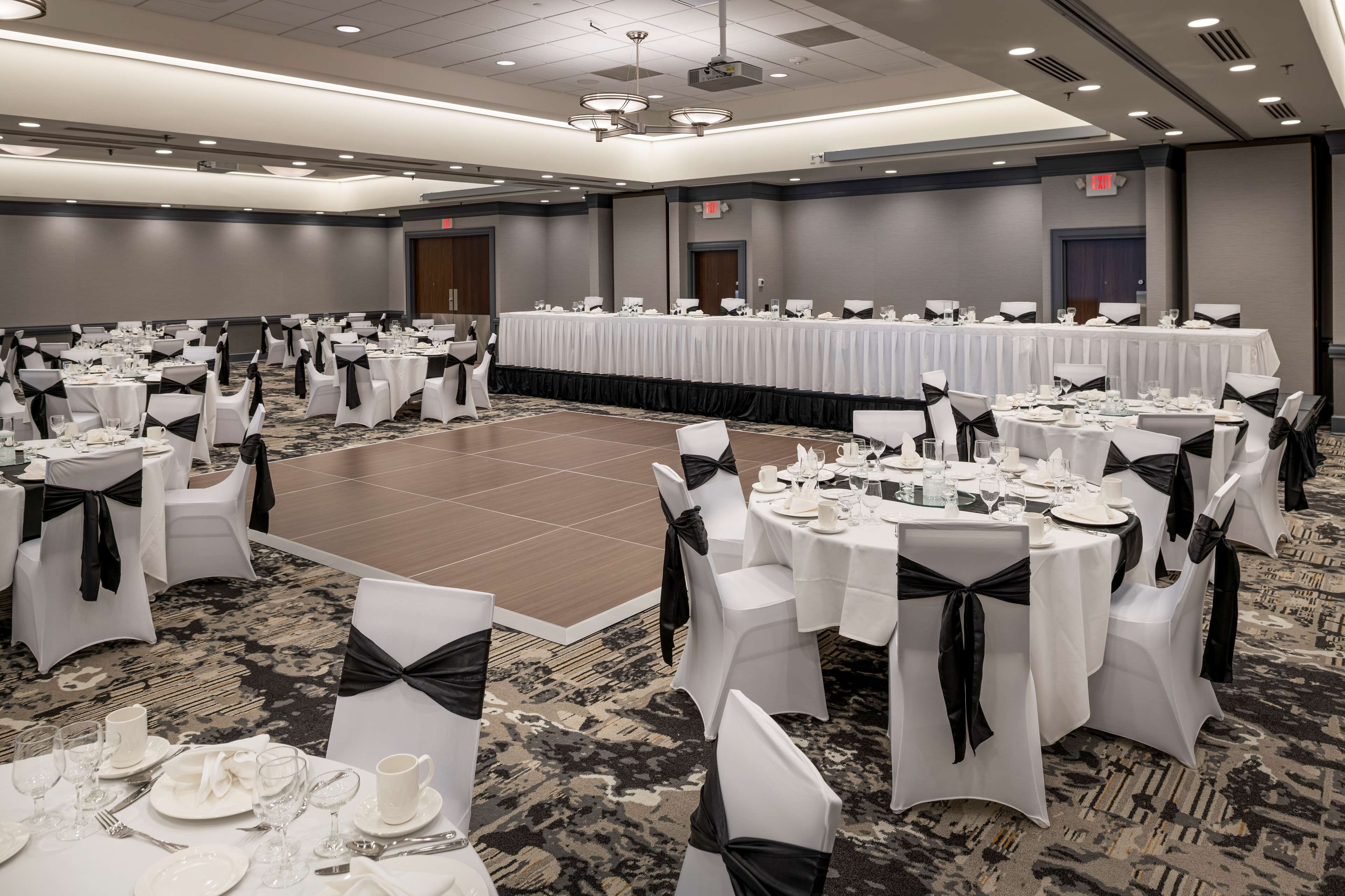A banquet hall with round tables, white tablecloths, and chairs with black sashes.