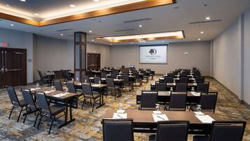A conference room with multiple tables and chairs, a projector screen displaying "DoubleTree by Hilton", and a carpeted floor.