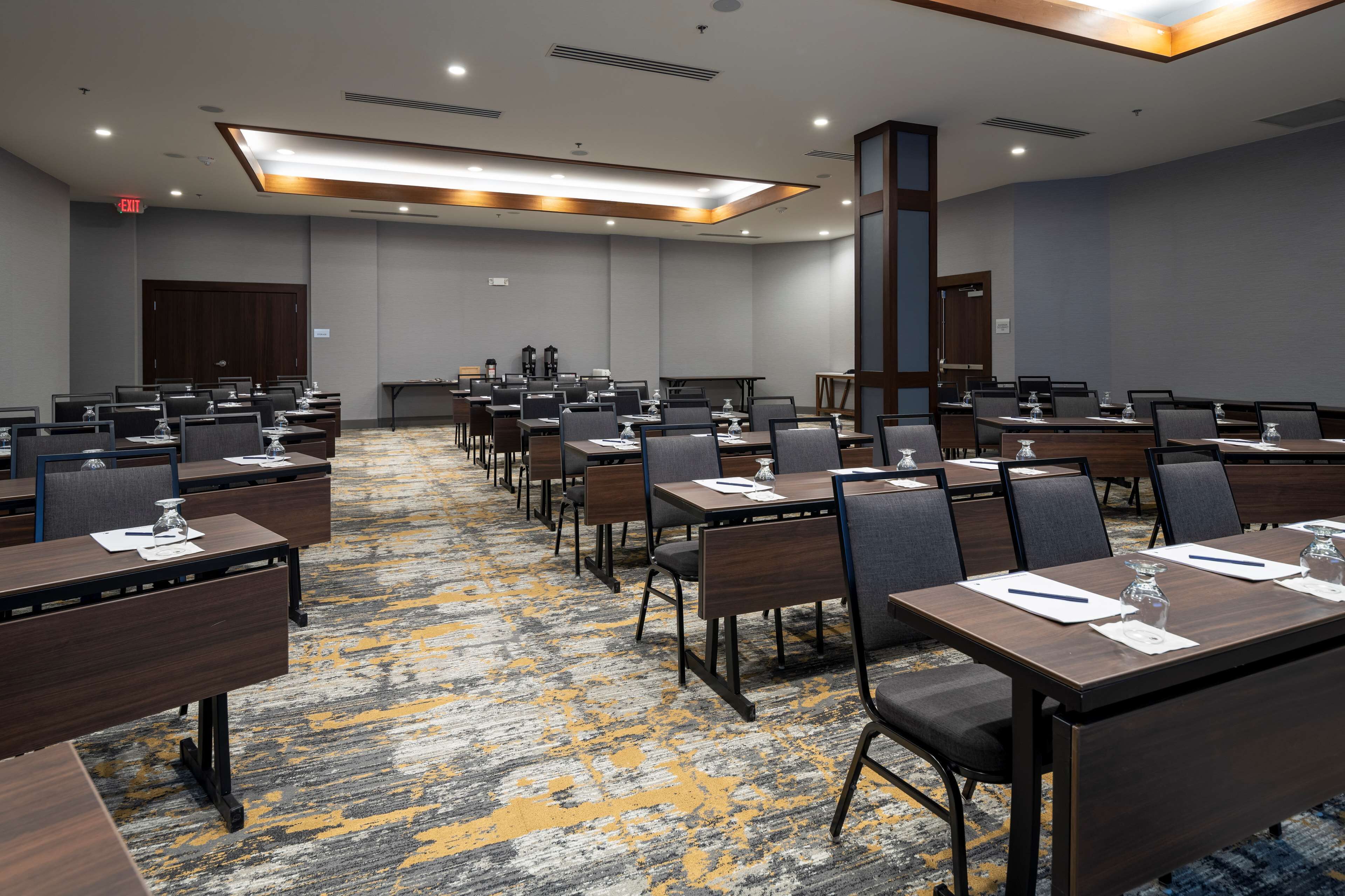 Un salón de conferencias con varias mesas y sillas, equipado con botellas de agua y blocs de notas.