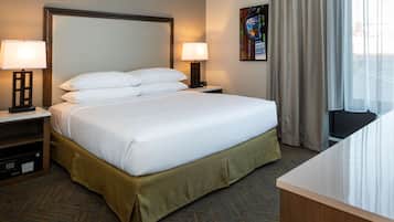 A hotel room with a large bed, two bedside tables with lamps, a carpeted floor, and a window with curtains.